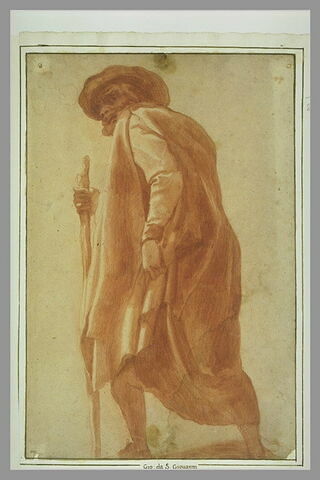 Homme drapé dans un manteau, coiffé d'un chapeau, appuyé sur un bâton et marchant vers la gauche