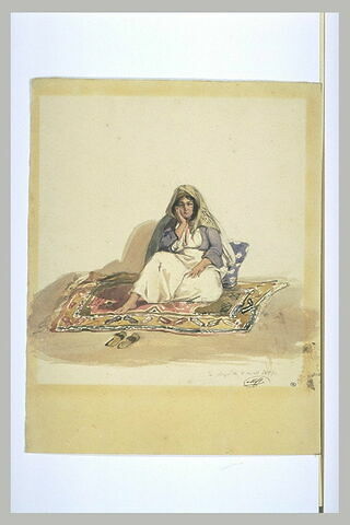 Femme syrienne assise sur un tapis d'Orient et sur un coussin bleu à fleurs