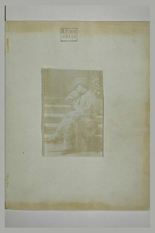 Homme assis sur une chaise, devant un escalier, la tête appuyée sur un bras, image 1/1