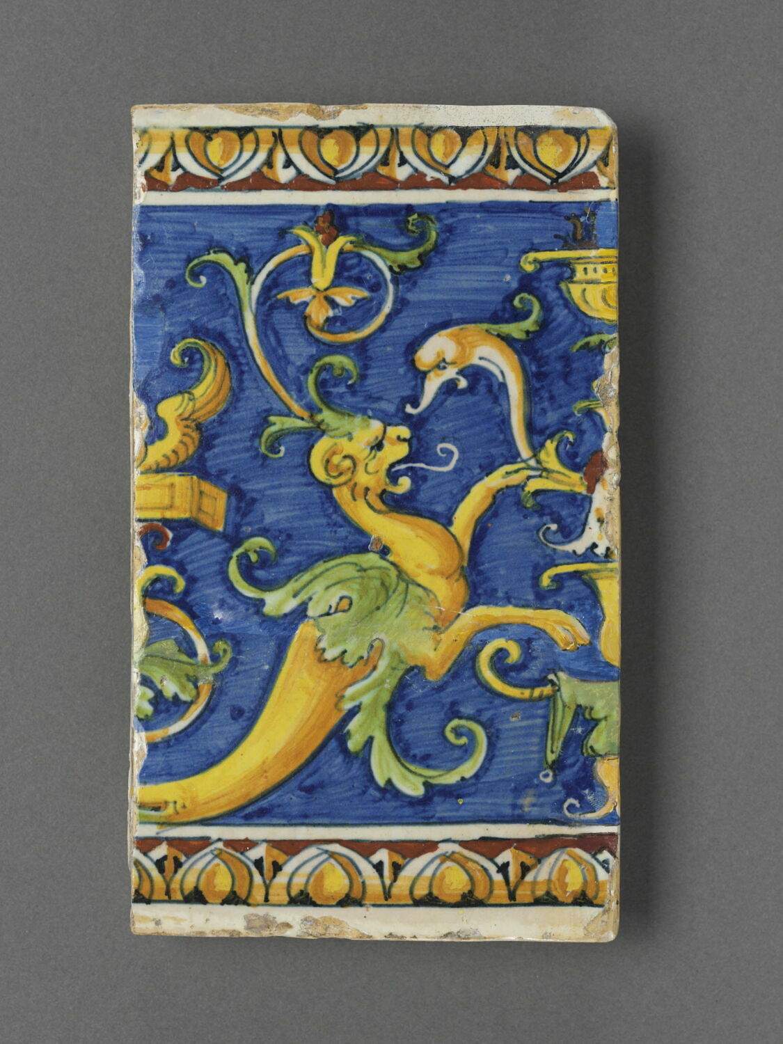 Carreau rectangulaire - pavé de bordure : décor de grotesques sur fond bleu