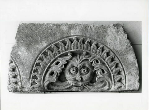 Fragment de tympan décoré de deux motifs semi-circulaires ornés d'un masque grotesque de la bouche duquel s'échappent des feuillages