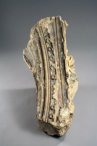 Fragment d'arcature sculpté sur quatre faces, décoré d'une tête encapuchonnée à pattes griffues