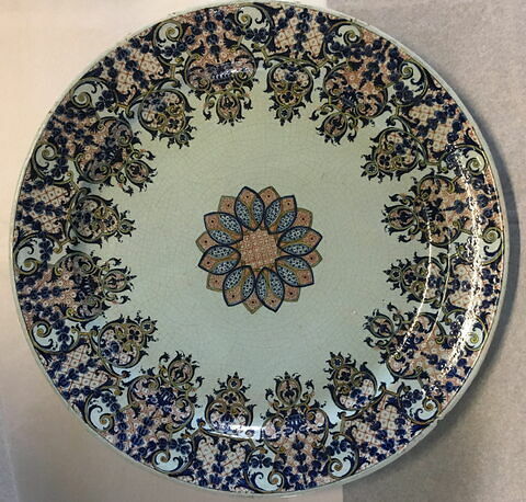 Grand plat circulaire en faïence, décor bleu et rouge de lambrequin au marli, et d'une rosace au centre.