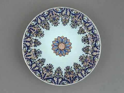 Grand plat circulaire en faïence, décor bleu et rouge de lambrequin au marli, et d'une rosace au centre.