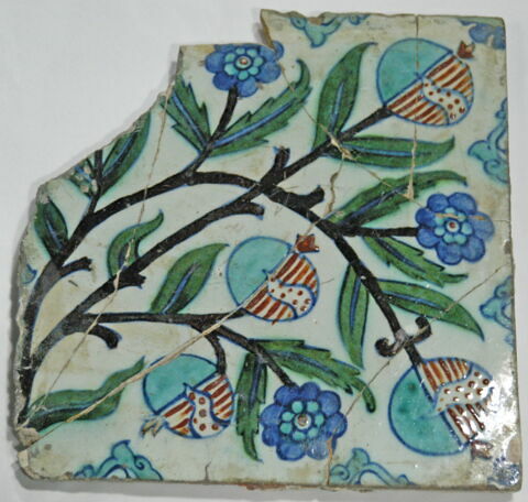 Carreau écorné, cassé et recollé en plusieurs endroits. Branches de grenadiers portant des fleurs et des grenades (des grenades mûres dont on voit les pépins) mi-turquoise, mi-rayé rouge et blanc, image 1/1
