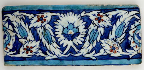 Carreau de bordure à décor de palmettes feuillues et de feuilles dentelées décorées de tulipes sur fond bleu