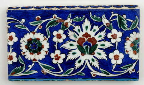 Carreau de bordure aux lotus alternant avec des fleurettes et des rosettes sur fond bleu
