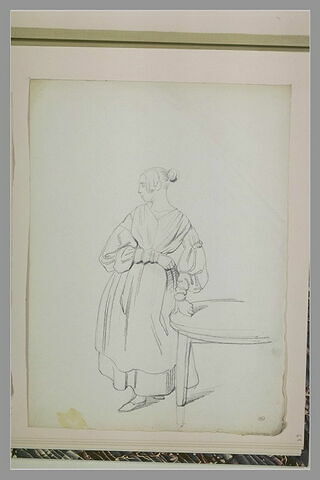 Femme debout, la main gauche posée sur une table, image 1/1
