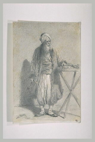 Vieil oriental à turban, barbu, debout, la main gauche appuyée sur une table