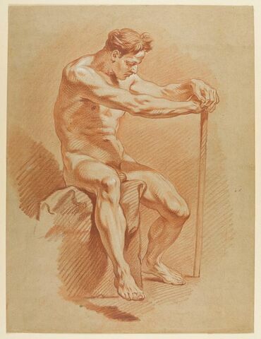 Homme assis sur un rocher, les mains appuyées sur un bâton, image 1/2
