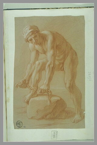 Un homme nu debout, le pied sur un rocher, nouant une corde à sa cheville, image 1/1