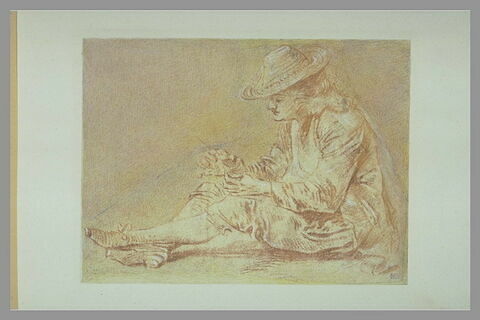 Homme assis à terre, de profil vers la gauche, un brin d'herbe dans la main