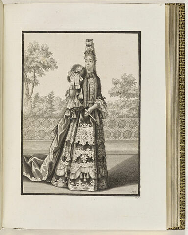 Une femme debout devant une balustrade, portant un manchon et un éventail dans ses mains, image 1/1